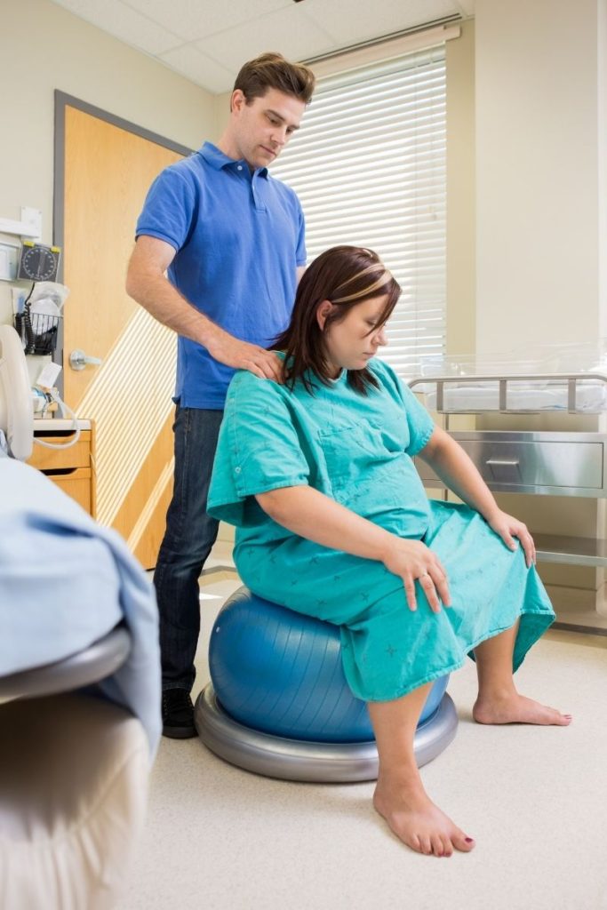 pregnant woman sitting on birth ball with man standing behind her rubbing her shoulders