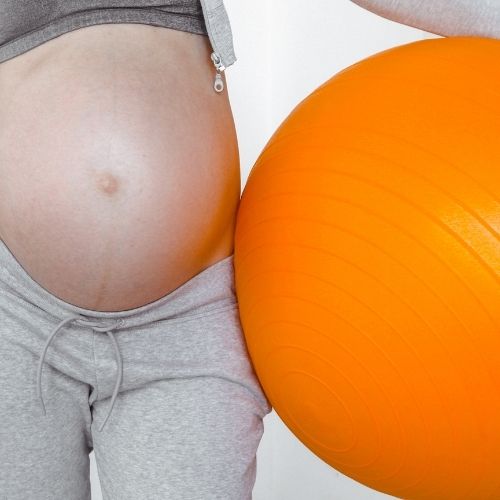 pregnant woman holding orange birth ball against hips
