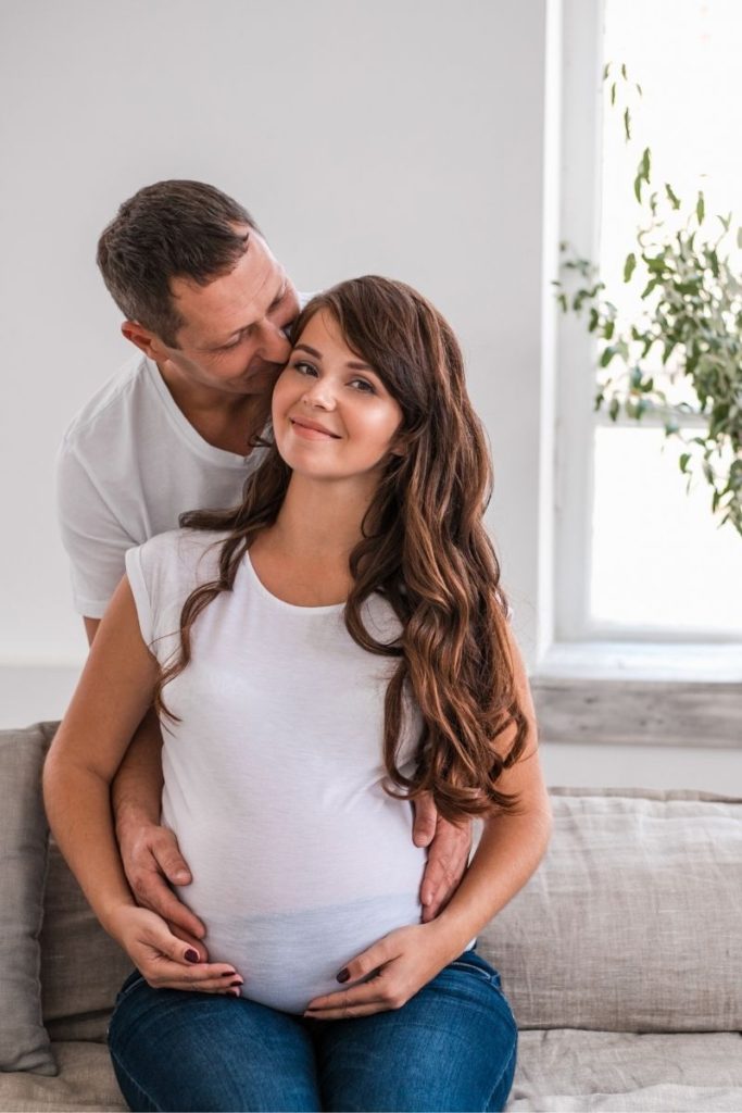 pregnant woman holding belly with man kissing her cheek