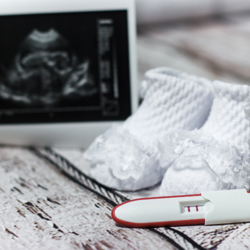 A pregnancy test sitting in front of baby shoes and ultrasound photo