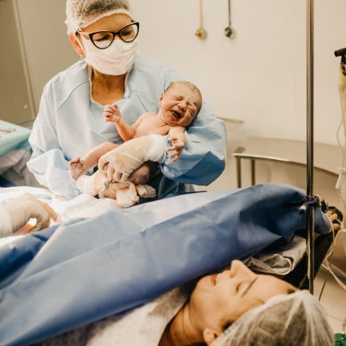 c-section doctor holding baby with surgical drape lowered