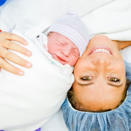 woman smiling next to swaddled baby while on operating table