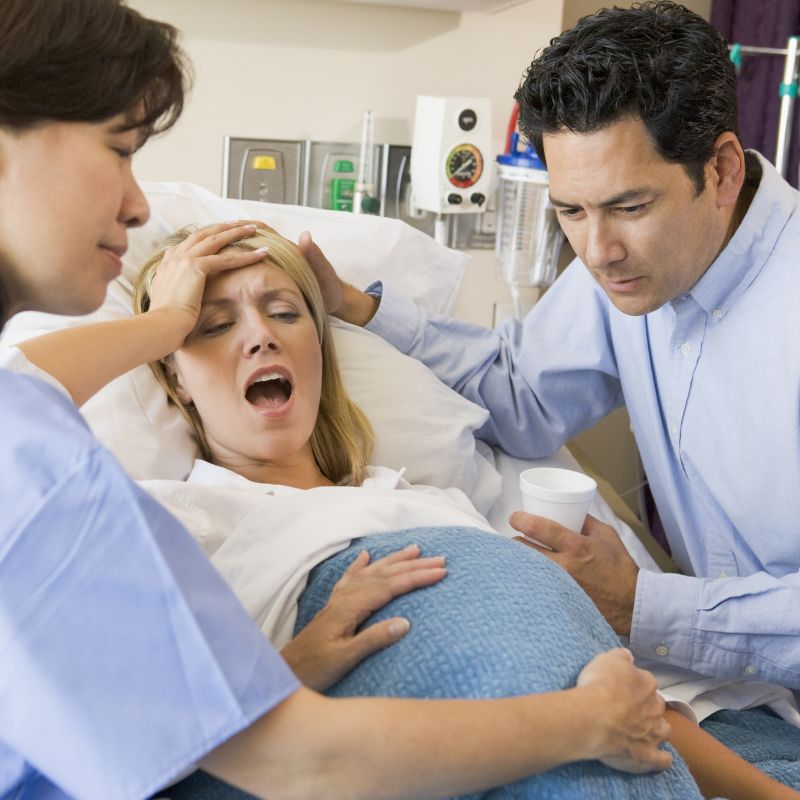 pregnant person in bed wincing with man and woman touching her forehead and belly